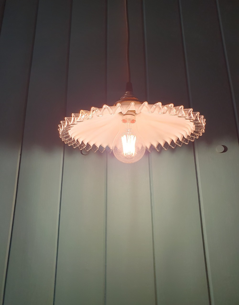 A white opaline glass pendant lampshade featuring a clear crimped frill edge suspended from a brass fixture. View II