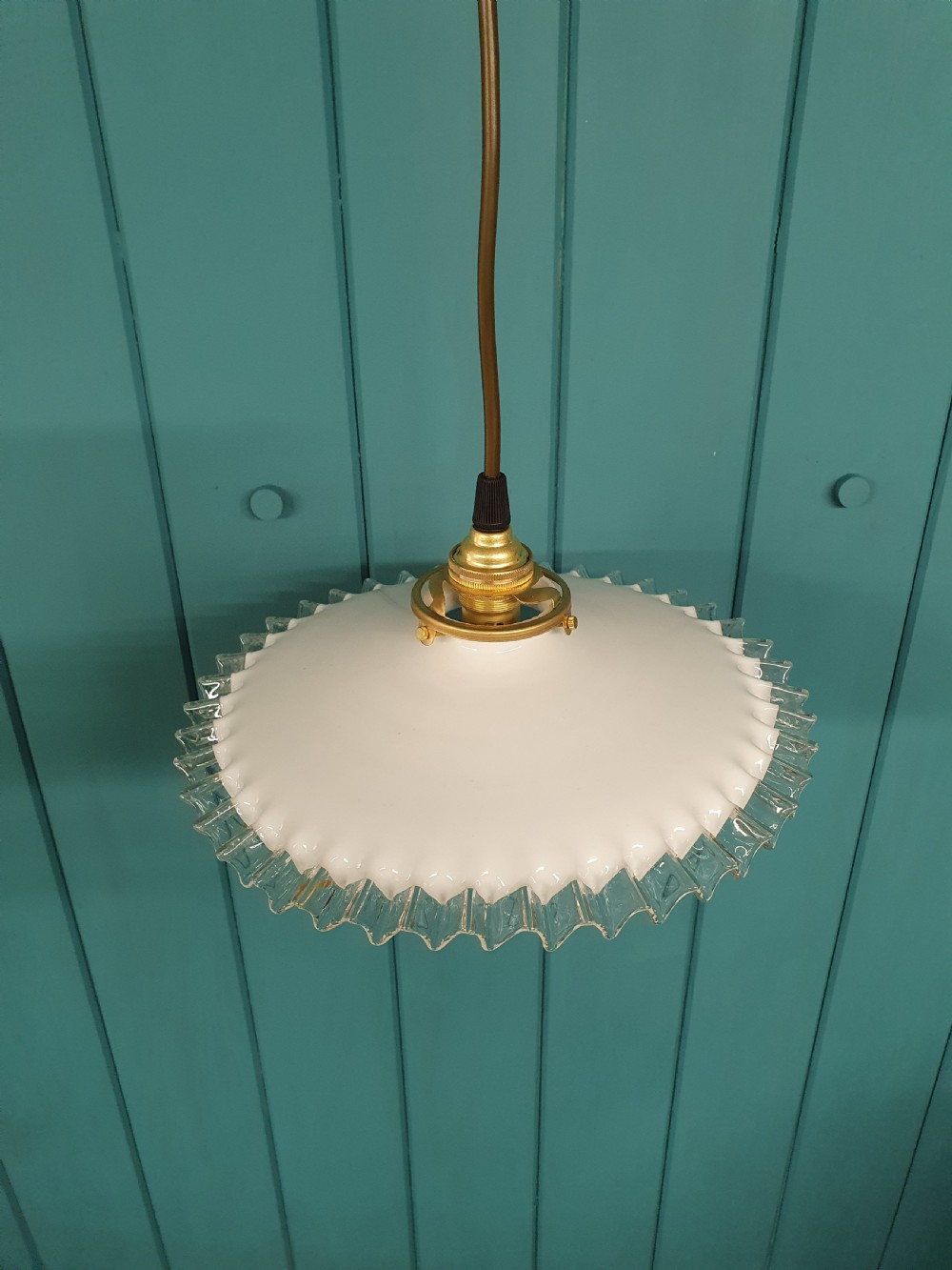 A white opaline glass pendant lampshade featuring a clear crimped frill edge suspended from a brass fixture. View III