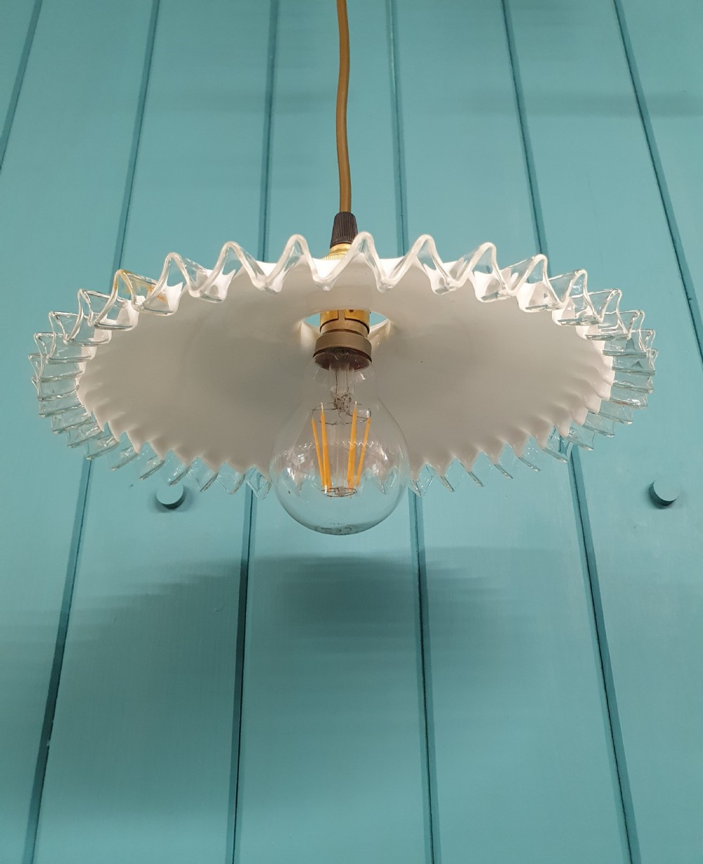 A white opaline glass pendant lampshade featuring a clear crimped frill edge suspended from a brass fixture. View IV