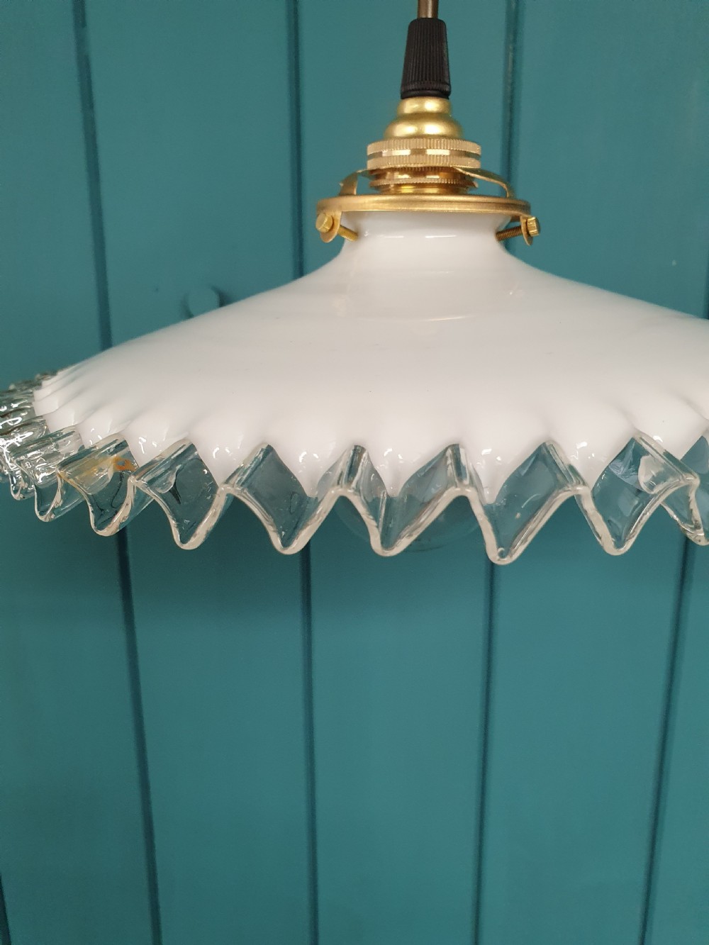 A white opaline glass pendant lampshade featuring a clear crimped frill edge suspended from a brass fixture. View V