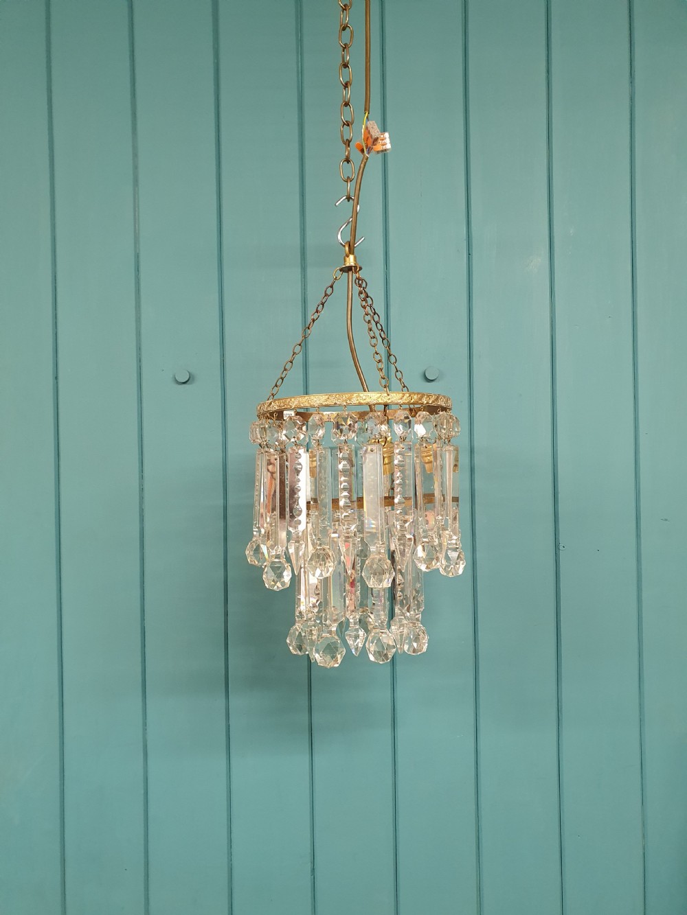 A small early 20th-century ceiling chandelier featuring a decorative brass gallery with tiered, clear glass prism drops hanging from thin metal chains.