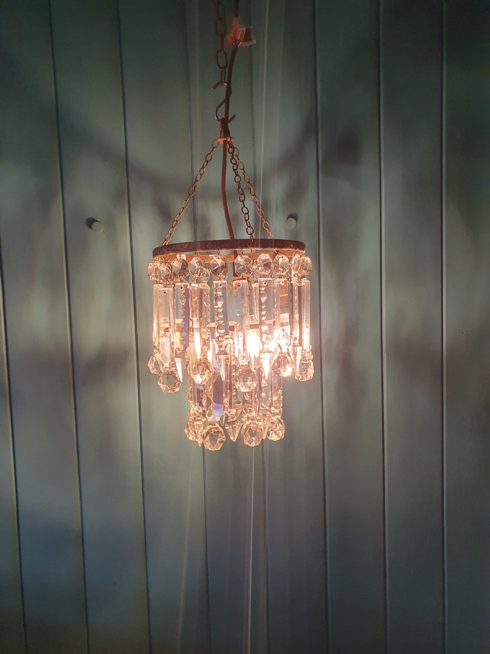 A small early 20th-century ceiling chandelier featuring a decorative brass gallery with tiered, clear glass prism drops hanging from thin metal chains. View II