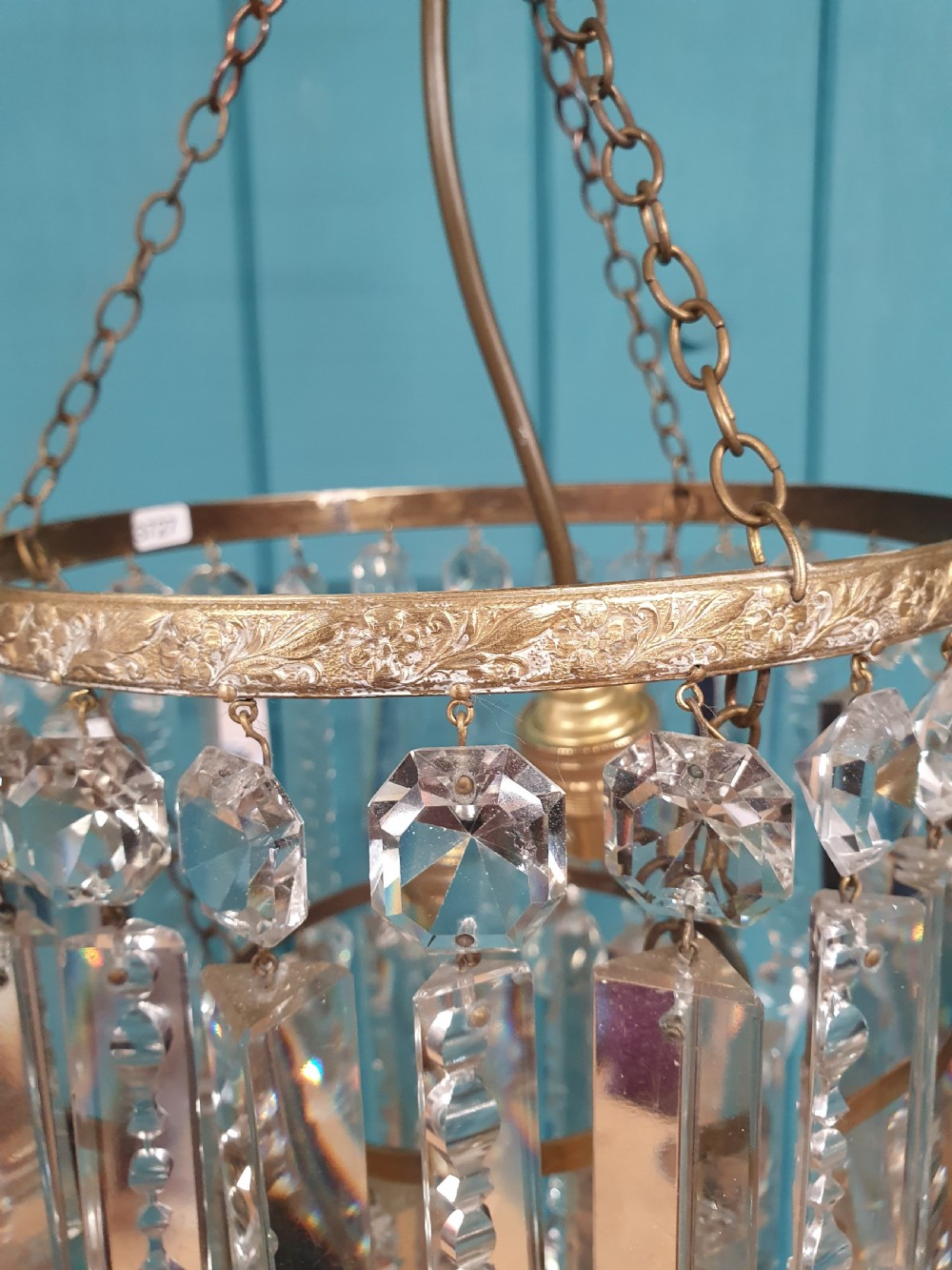 A small early 20th-century ceiling chandelier featuring a decorative brass gallery with tiered, clear glass prism drops hanging from thin metal chains. View III