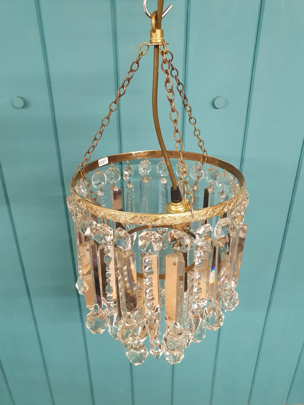 A small early 20th-century ceiling chandelier featuring a decorative brass gallery with tiered, clear glass prism drops hanging from thin metal chains. View V