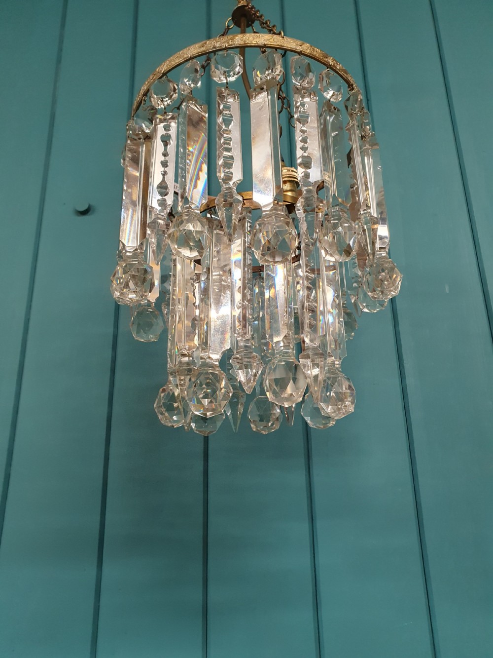A small early 20th-century ceiling chandelier featuring a decorative brass gallery with tiered, clear glass prism drops hanging from thin metal chains. View VI