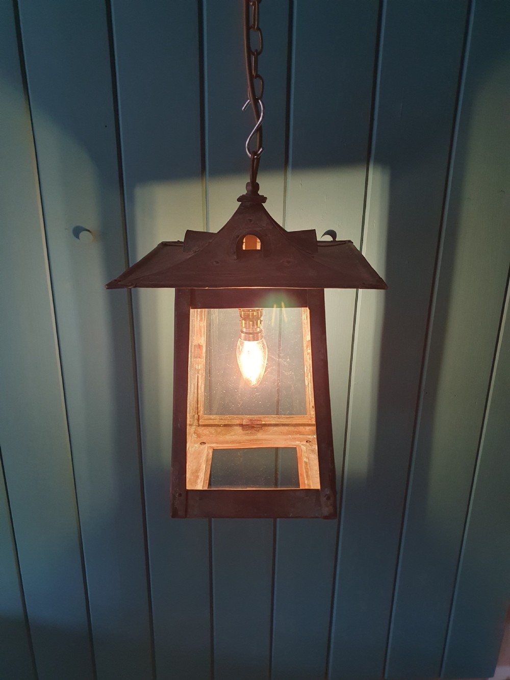 An early 20th-century patinated brass pendant lantern with clear glass side panels suspended by a chain. View II