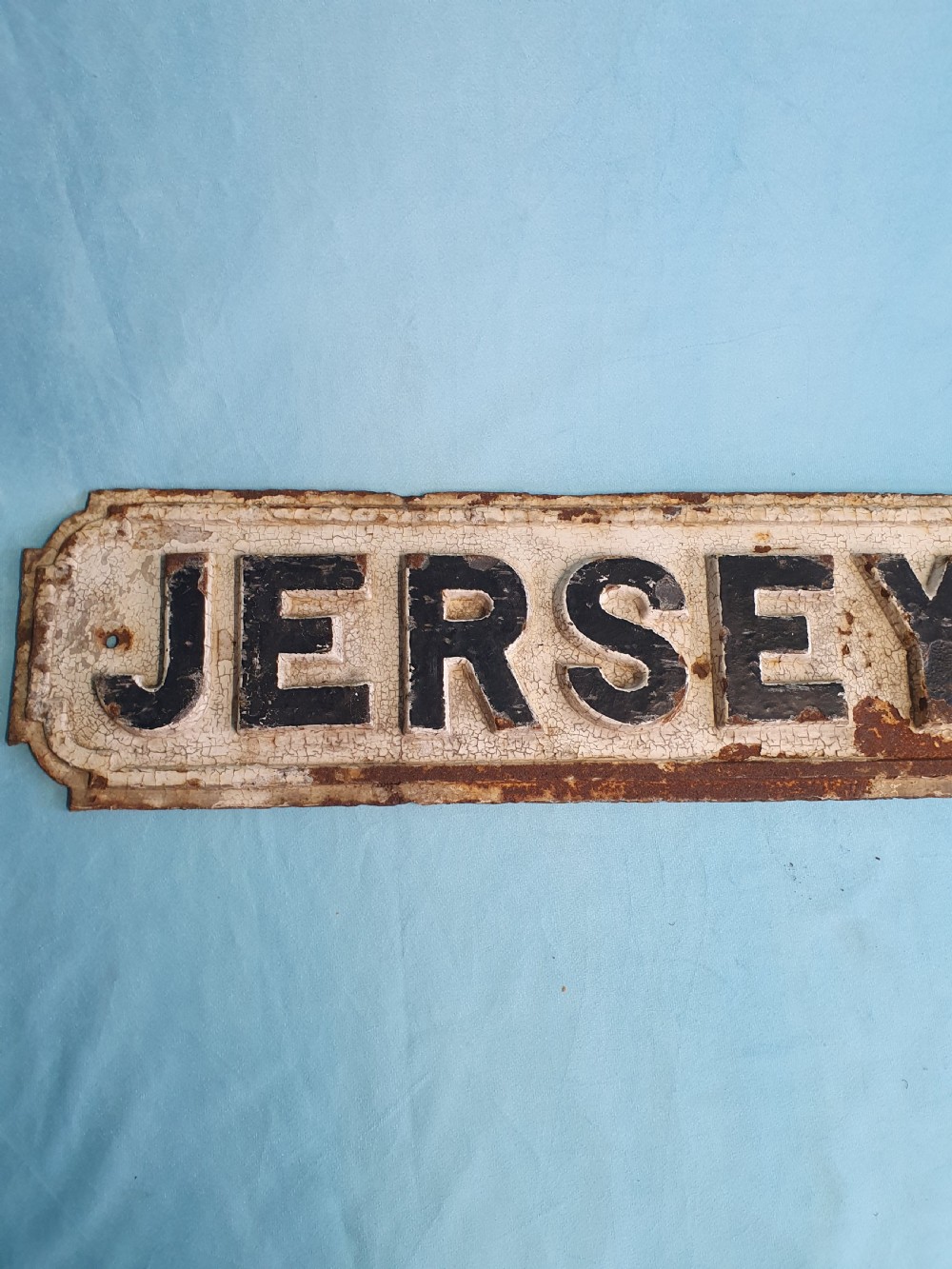 A late nineteenth-century rectangular cast iron street sign featuring raised black lettering reading JERSEY ROAD against a weathered off-white painted background. View VI