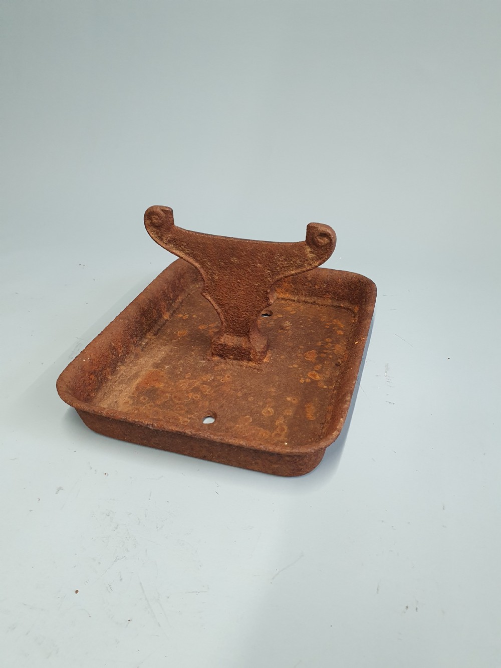A late nineteenth-century cast iron boot scraper featuring a rectangular drip tray base and a scroll-detailed scraping blade with heavy rusted patina.