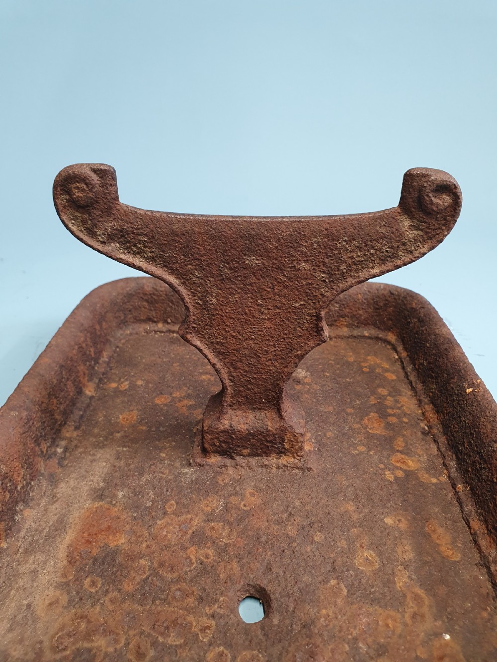 A late nineteenth-century cast iron boot scraper featuring a rectangular drip tray base and a scroll-detailed scraping blade with heavy rusted patina. View II