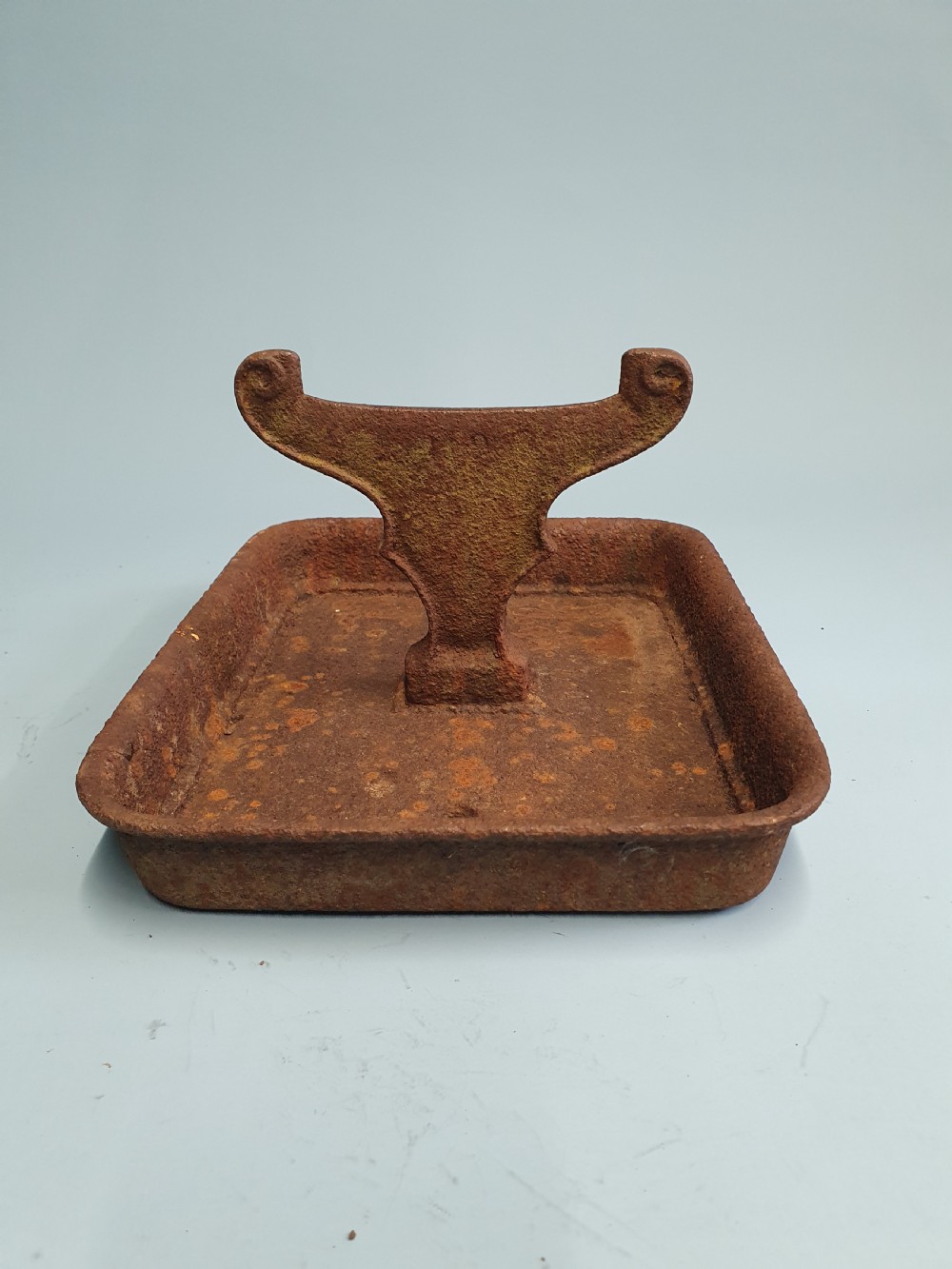A late nineteenth-century cast iron boot scraper featuring a rectangular drip tray base and a scroll-detailed scraping blade with heavy rusted patina. View VI