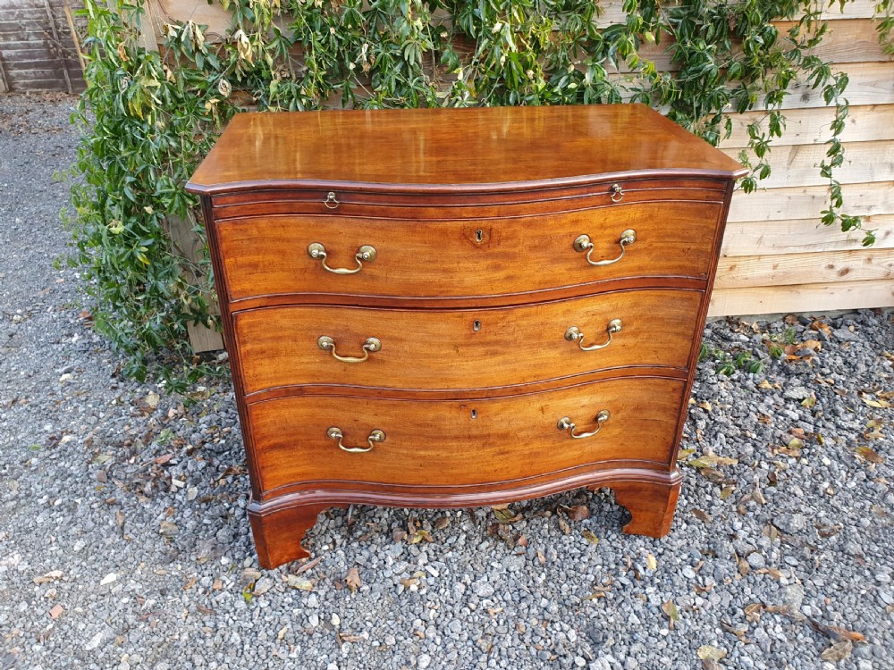 A Georgian mahogany serpentine chest of drawers featuring a curved three-drawer front, brass swan-neck handles, and shaped bracket feet.