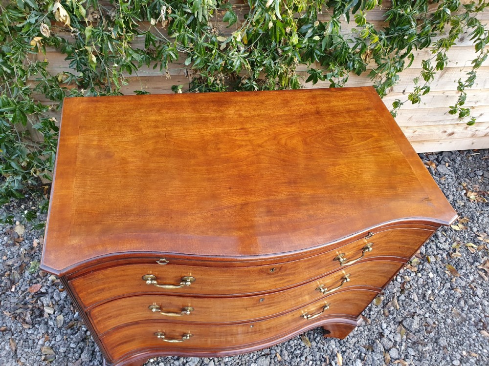 A Georgian mahogany serpentine chest of drawers featuring a curved three-drawer front, brass swan-neck handles, and shaped bracket feet. View II