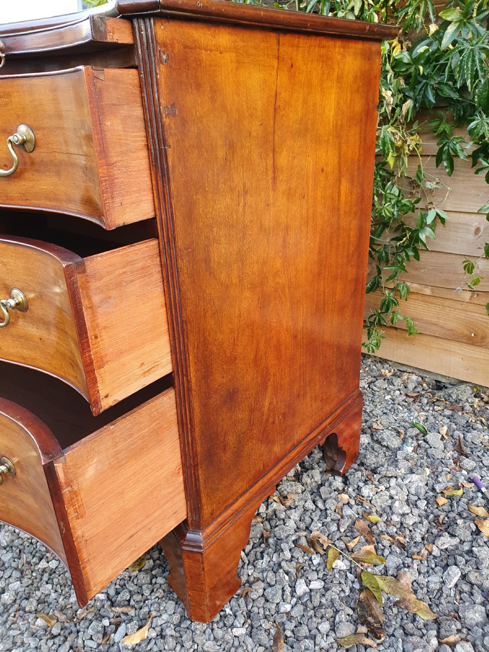 A Georgian mahogany serpentine chest of drawers featuring a curved three-drawer front, brass swan-neck handles, and shaped bracket feet. View III