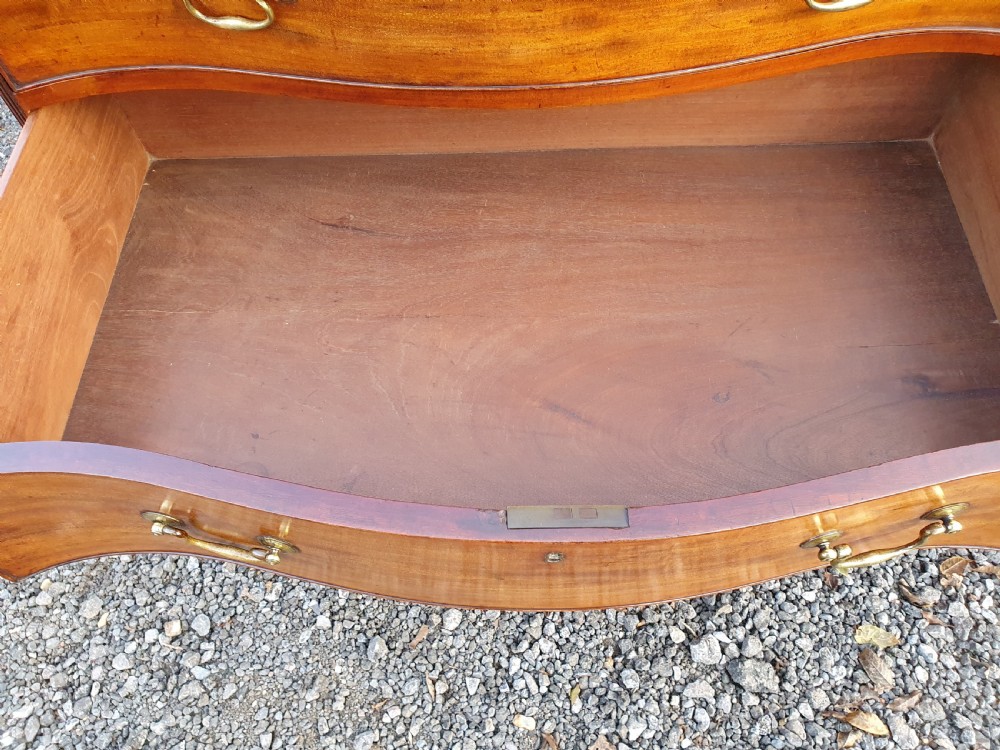 A Georgian mahogany serpentine chest of drawers featuring a curved three-drawer front, brass swan-neck handles, and shaped bracket feet. View VII