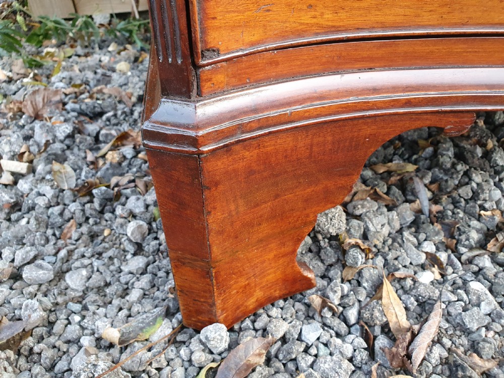 A Georgian mahogany serpentine chest of drawers featuring a curved three-drawer front, brass swan-neck handles, and shaped bracket feet. View XI