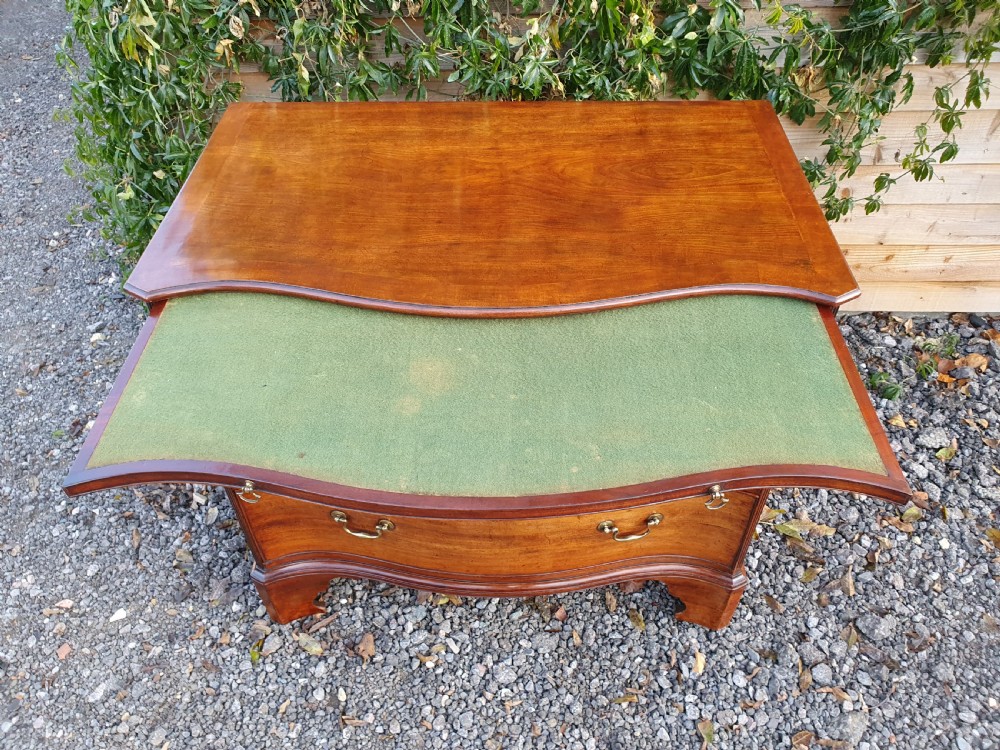 A Georgian mahogany serpentine chest of drawers featuring a curved three-drawer front, brass swan-neck handles, and shaped bracket feet. View XII