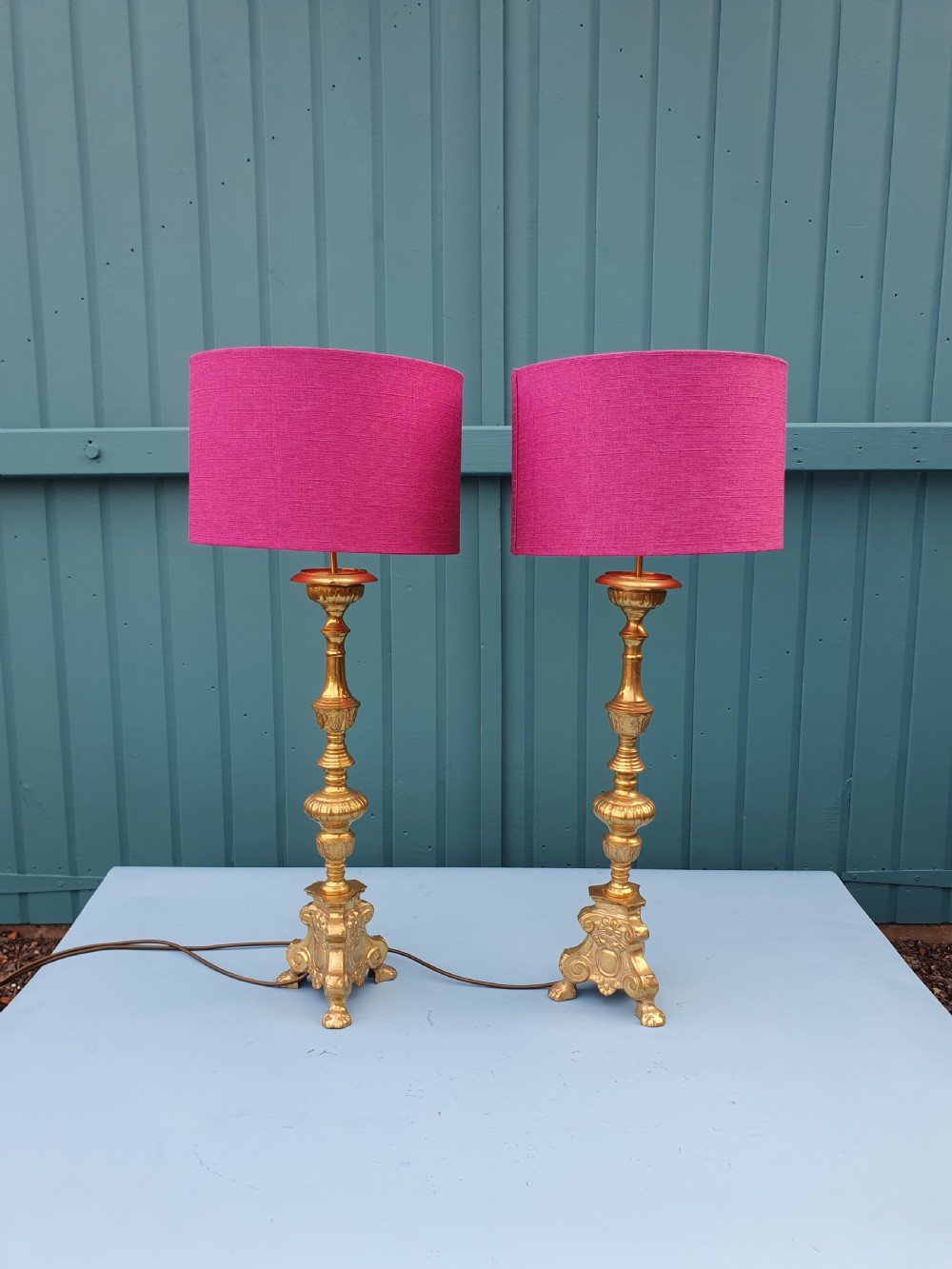 A pair of ornate cast brass candlestick-style table lamps fitted with bright pink fabric drum shades.
