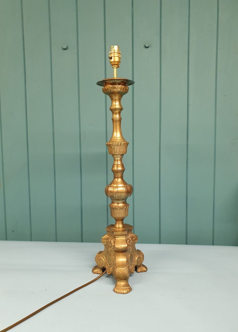 An early 20th-century Baroque revival cast brass candlestick table lamp with a scrolled tripod base and turned stem.