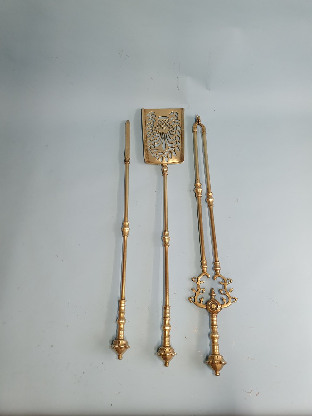 A three-piece set of 19th-century brass fire tools comprising a poker, tongs, and an ornamental shovel with a decorative pierced pattern.