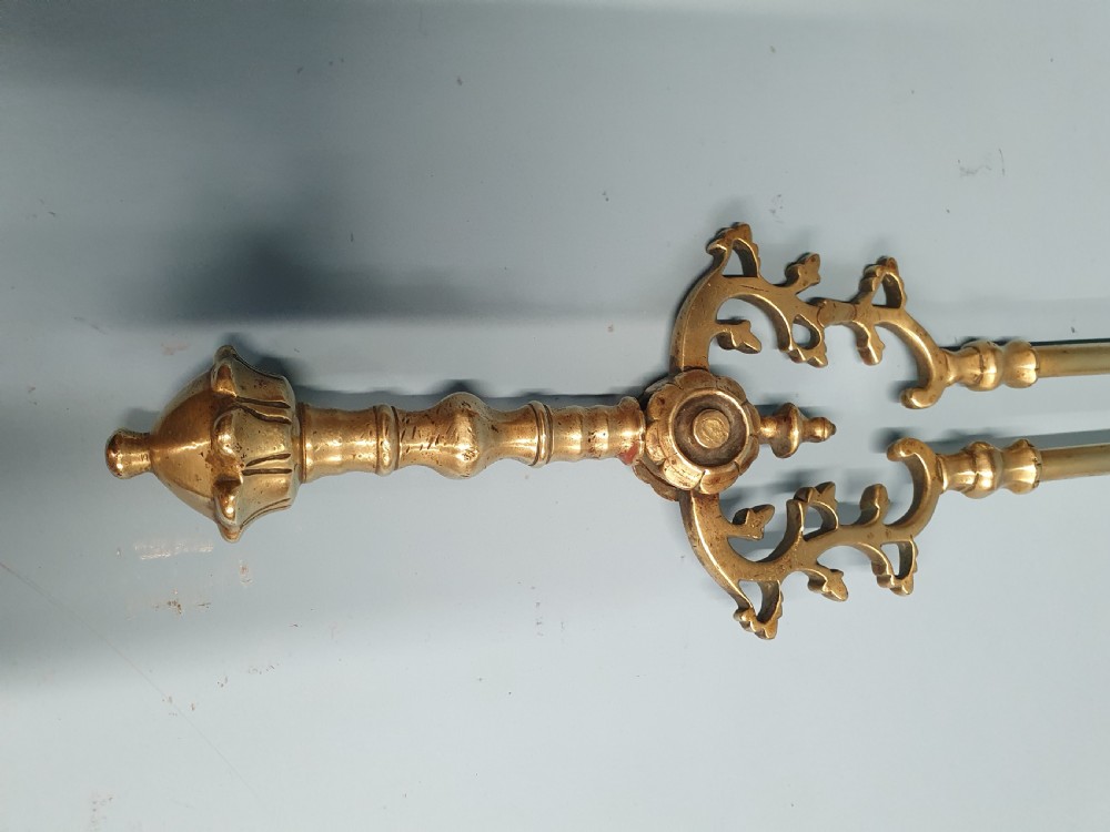 A three-piece set of 19th-century brass fire tools comprising a poker, tongs, and an ornamental shovel with a decorative pierced pattern. View III