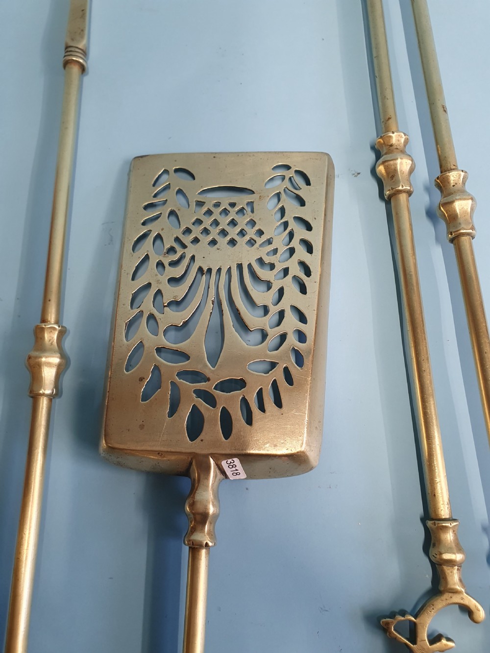 A three-piece set of 19th-century brass fire tools comprising a poker, tongs, and an ornamental shovel with a decorative pierced pattern. View V