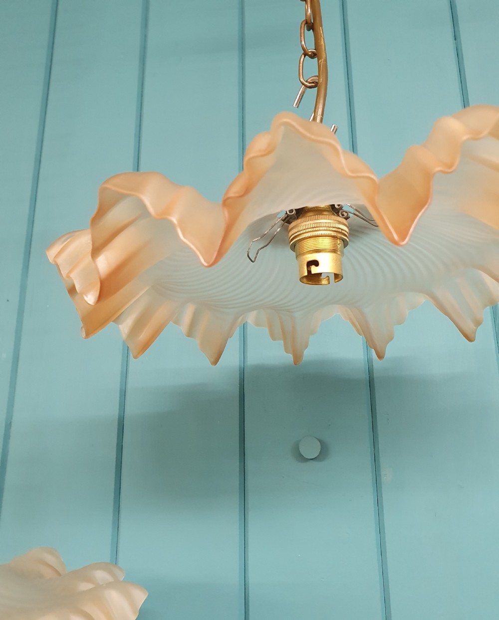 A pair of French pendant lights featuring peach frosted glass shades with ruffled fluted rims suspended from brass chains. View IV