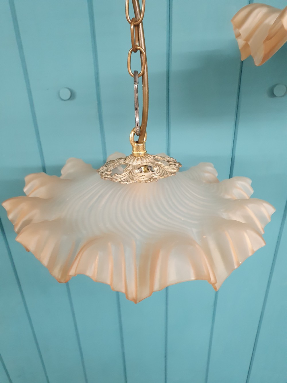 A pair of French pendant lights featuring peach frosted glass shades with ruffled fluted rims suspended from brass chains. View V