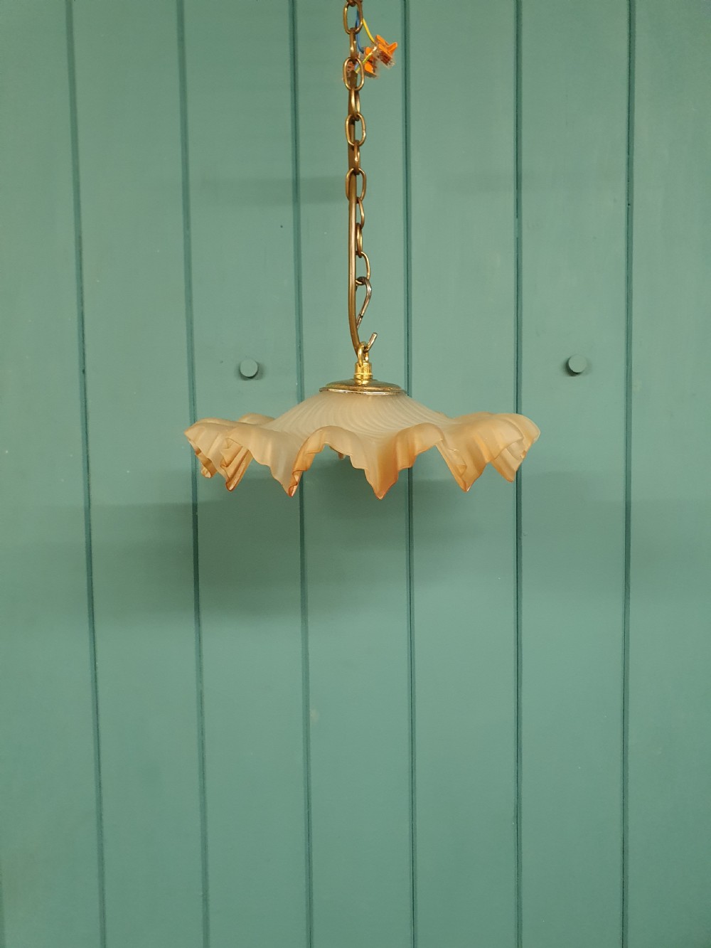 An antique French ceiling pendant featuring a frosted amber glass shade with a ruffled frilled rim suspended from a brass link chain.