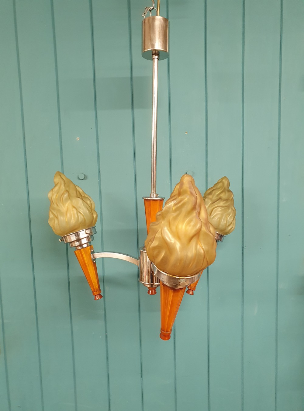 An Art Deco three-light chandelier featuring chrome stems, orange torch holders, and flame-shaped frosted glass shades.