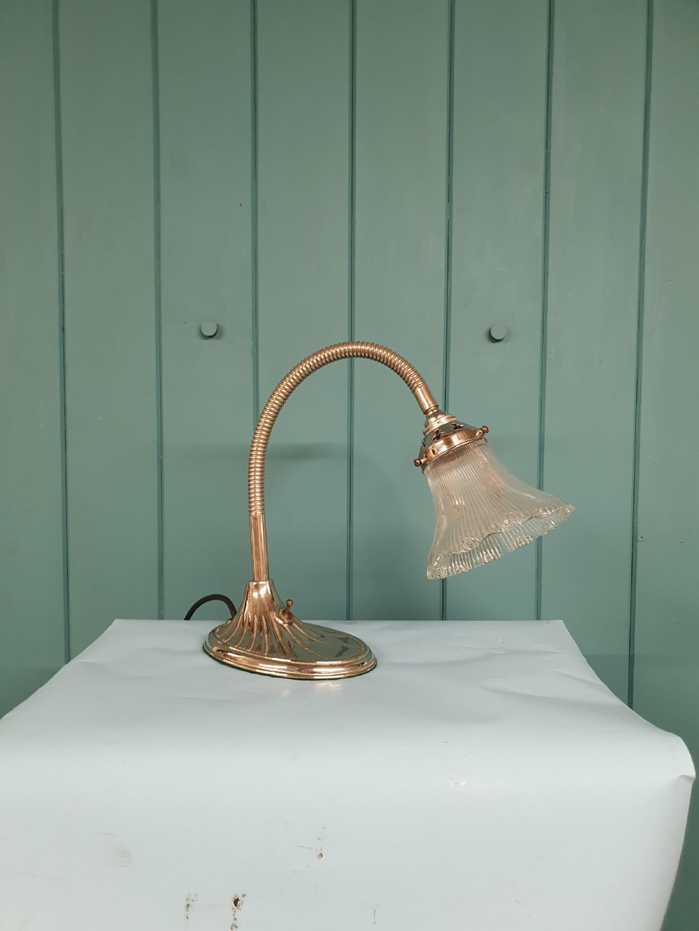 An Art Deco brass desk lamp featuring a shell-shaped base, flexible gooseneck arm, and a fluted clear glass shade. View VI