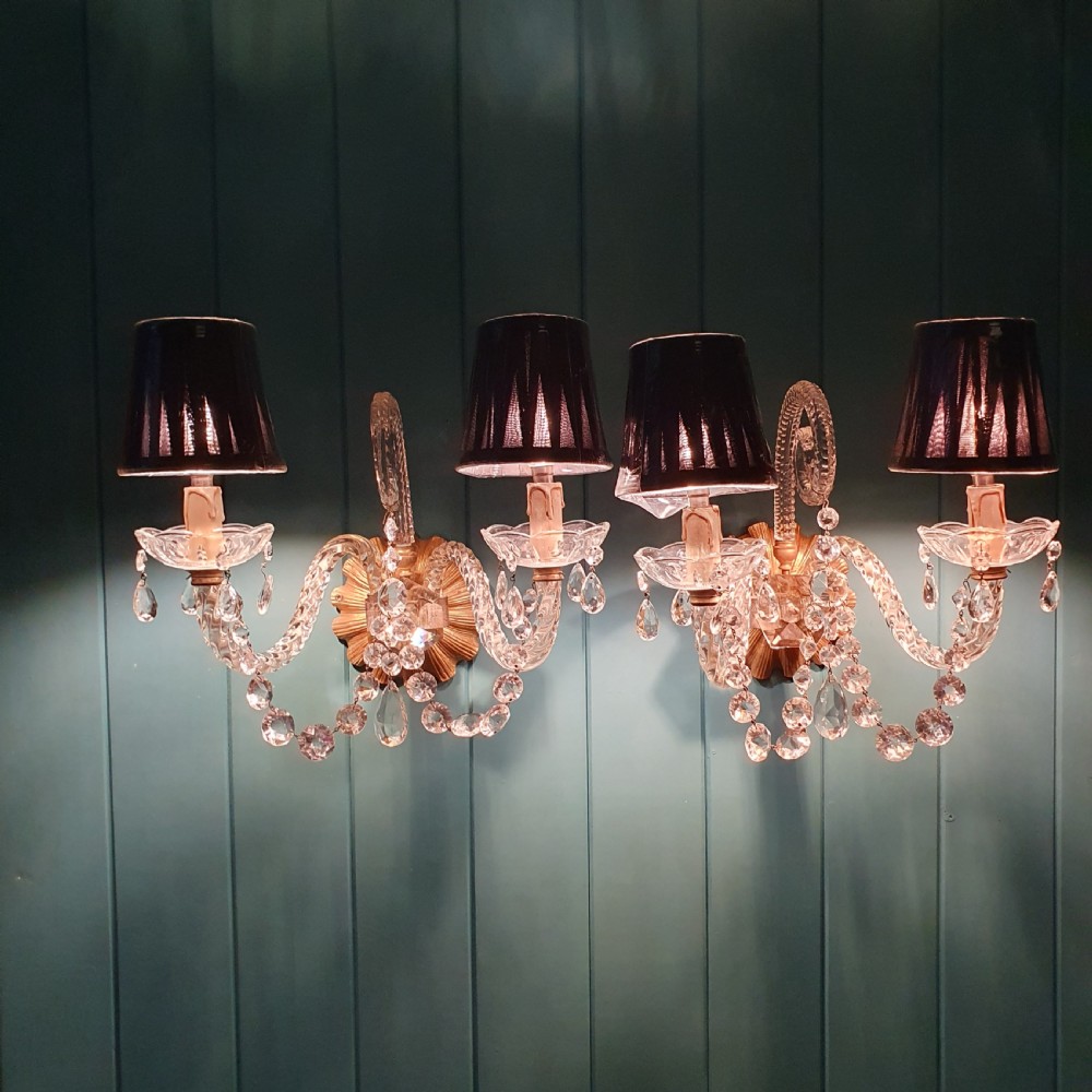 A pair of early 20th-century French double-arm glass wall sconces with crystal droplets, gilt brass backplates, and black lampshades. View V