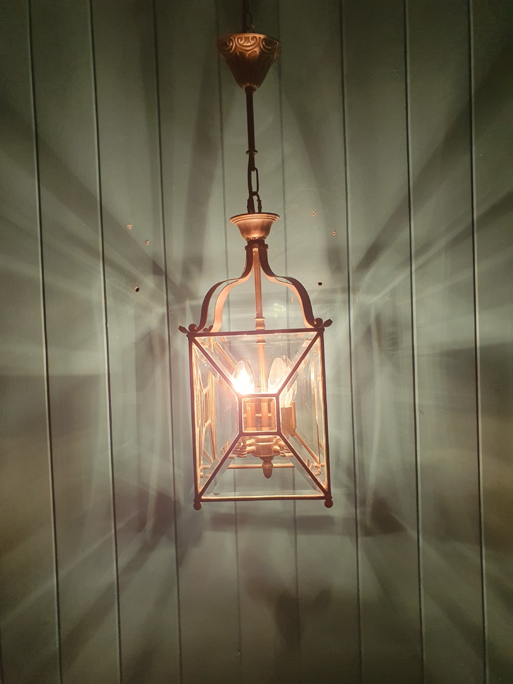 A square brass Arts and Crafts hall lantern featuring geometric bevelled glass panels suspended from a brass chain. View II