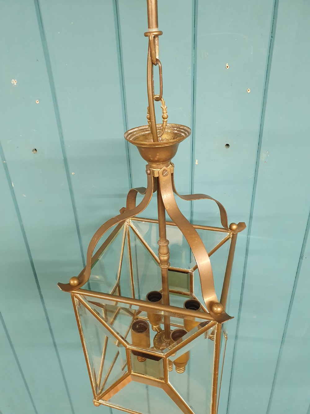 A square brass Arts and Crafts hall lantern featuring geometric bevelled glass panels suspended from a brass chain. View IV