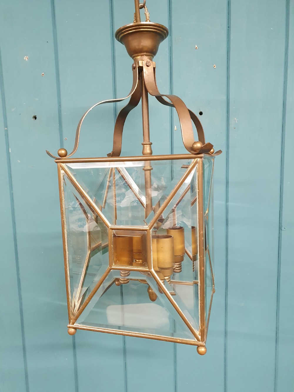 A square brass Arts and Crafts hall lantern featuring geometric bevelled glass panels suspended from a brass chain. View V
