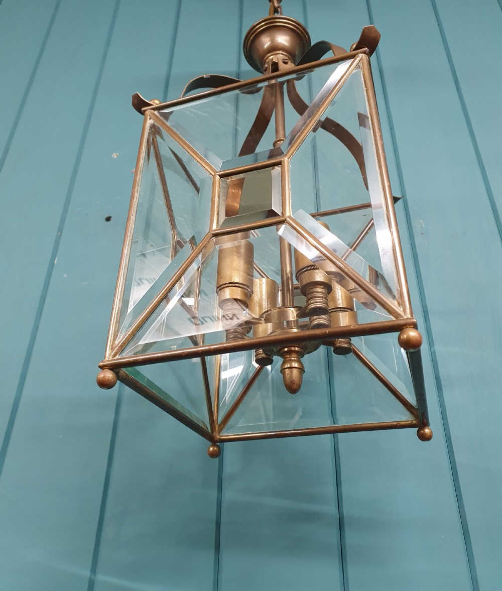A square brass Arts and Crafts hall lantern featuring geometric bevelled glass panels suspended from a brass chain. View VI