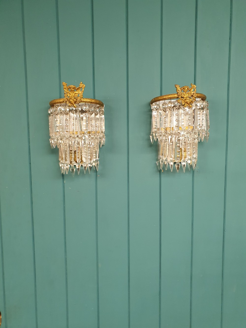 A pair of early 20th-century gilded brass wall sconces featuring top cherub figures and tiered hanging crystal prisms.
