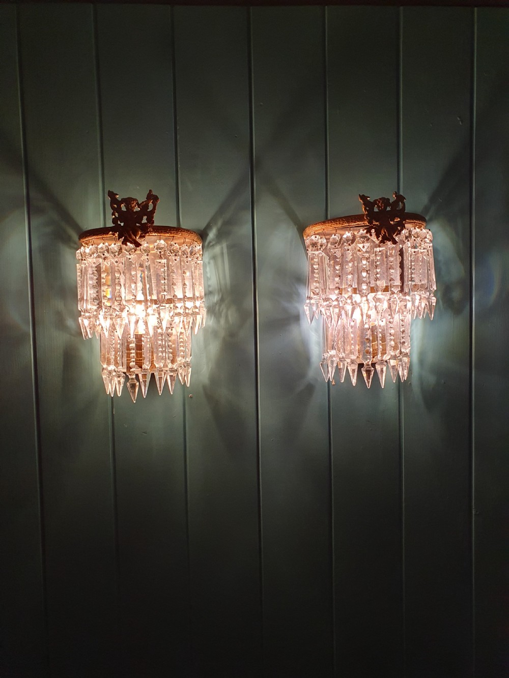 A pair of early 20th-century gilded brass wall sconces featuring top cherub figures and tiered hanging crystal prisms. View II