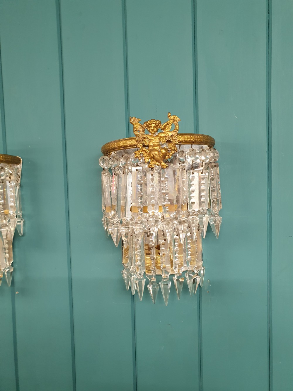 A pair of early 20th-century gilded brass wall sconces featuring top cherub figures and tiered hanging crystal prisms. View IV
