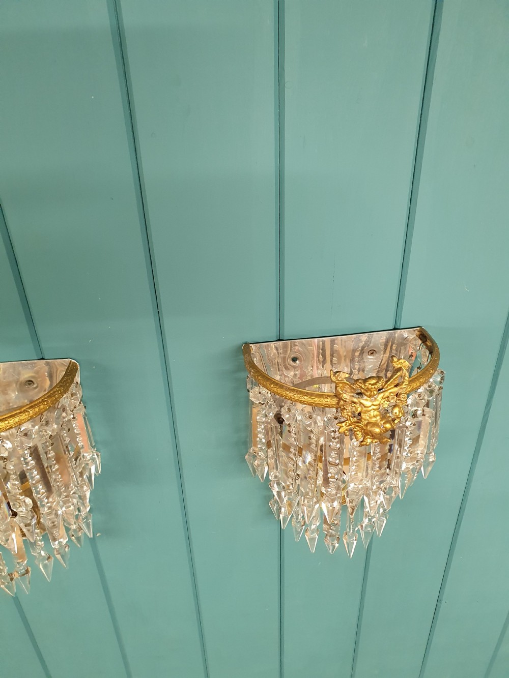 A pair of early 20th-century gilded brass wall sconces featuring top cherub figures and tiered hanging crystal prisms. View VI