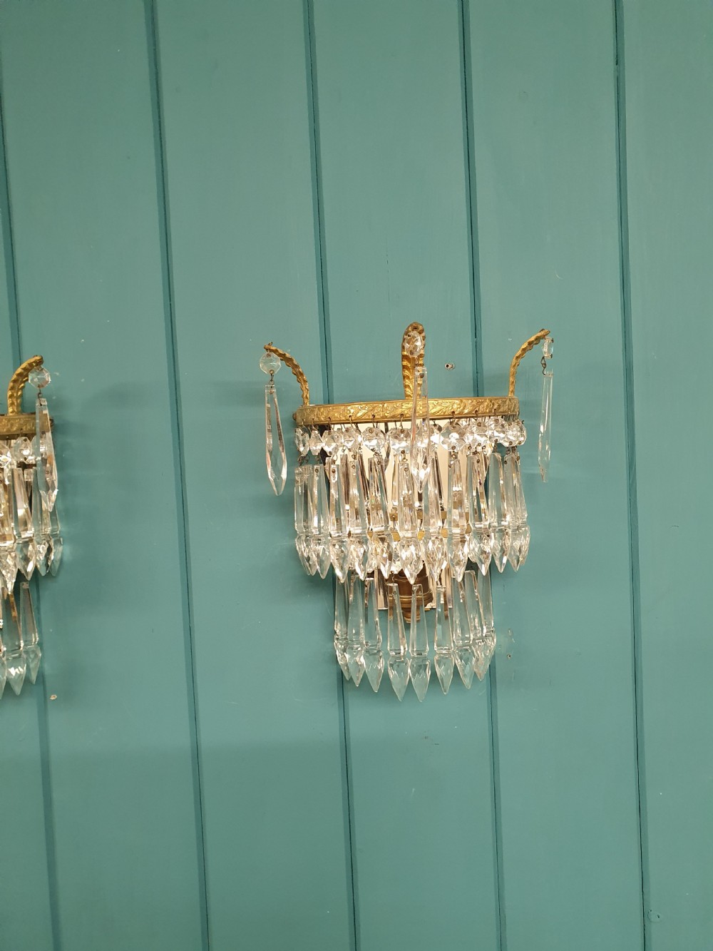 A pair of antique gilt brass wall lights featuring tiered crystal prisms, decorative top spikes, and mirrored backings. View III