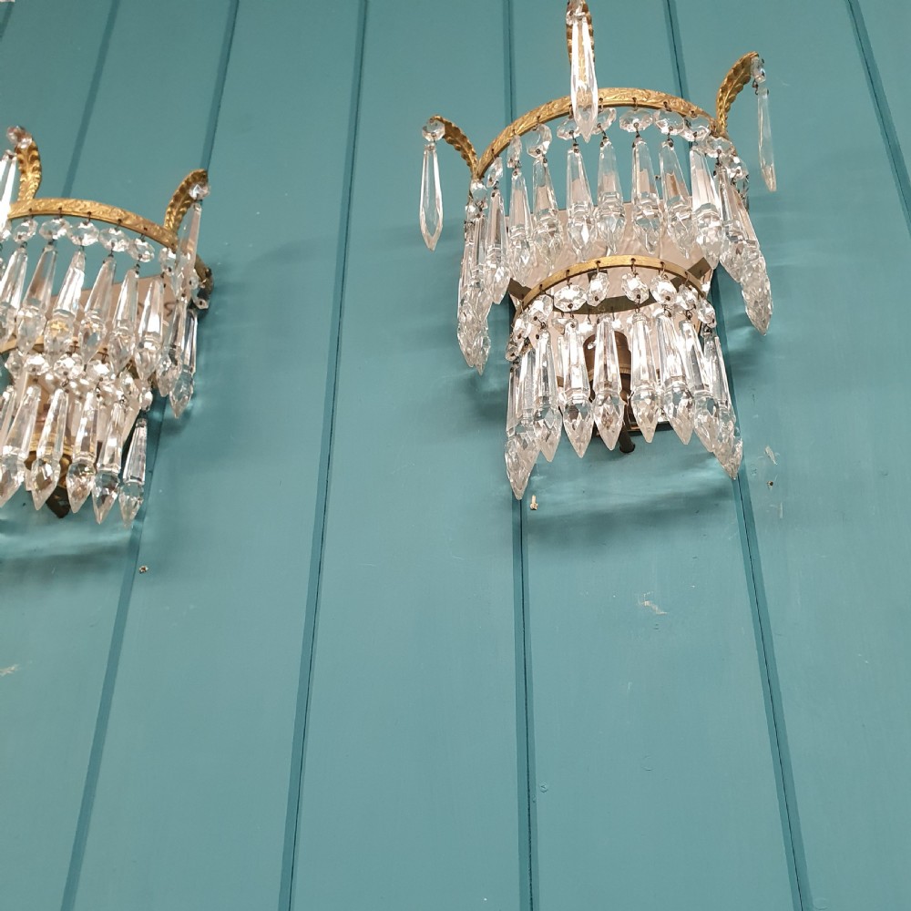 A pair of antique gilt brass wall lights featuring tiered crystal prisms, decorative top spikes, and mirrored backings. View IV