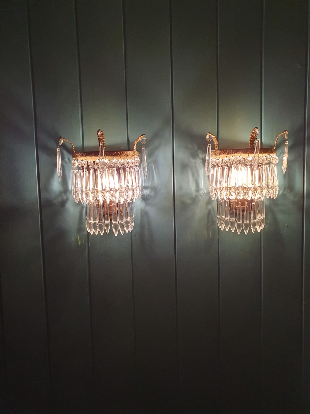 A pair of antique gilt brass wall lights featuring tiered crystal prisms, decorative top spikes, and mirrored backings. View V