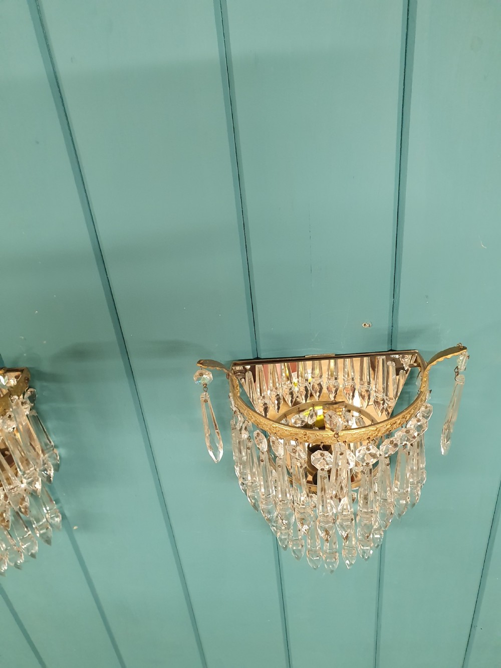 A pair of antique gilt brass wall lights featuring tiered crystal prisms, decorative top spikes, and mirrored backings. View VI