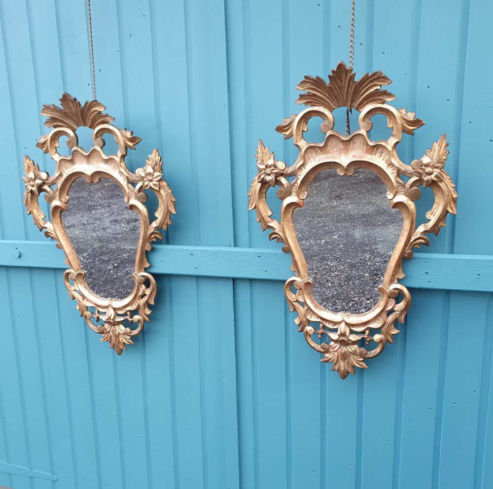 A matching pair of carved Italian Rococo style giltwood wall mirrors featuring leaf crests and elaborate floral scrollwork.