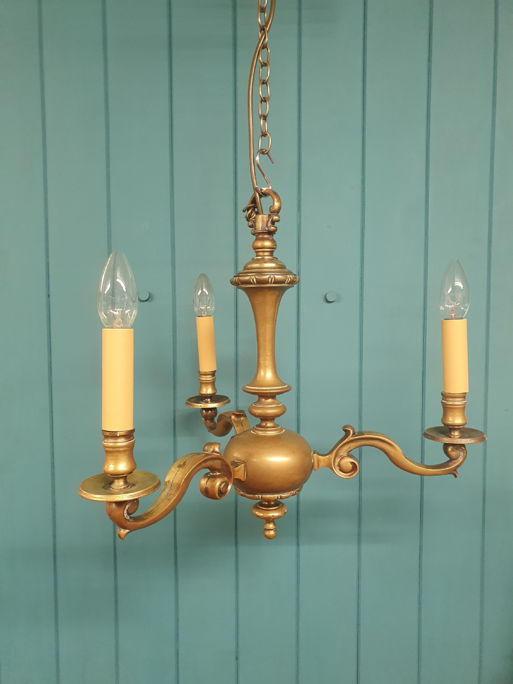 A three-arm Dutch Flemish style brass chandelier featuring a central turned baluster stem and s-scroll arms supporting faux candle sockets.