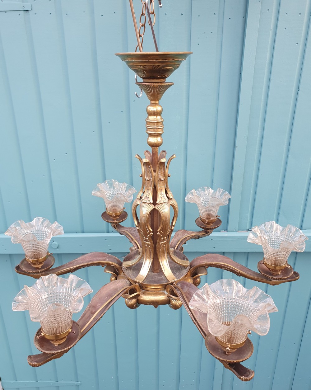 An early 20th-century six-arm brass ceiling chandelier featuring frilled clear glass shades and a central cast brass stem. View X