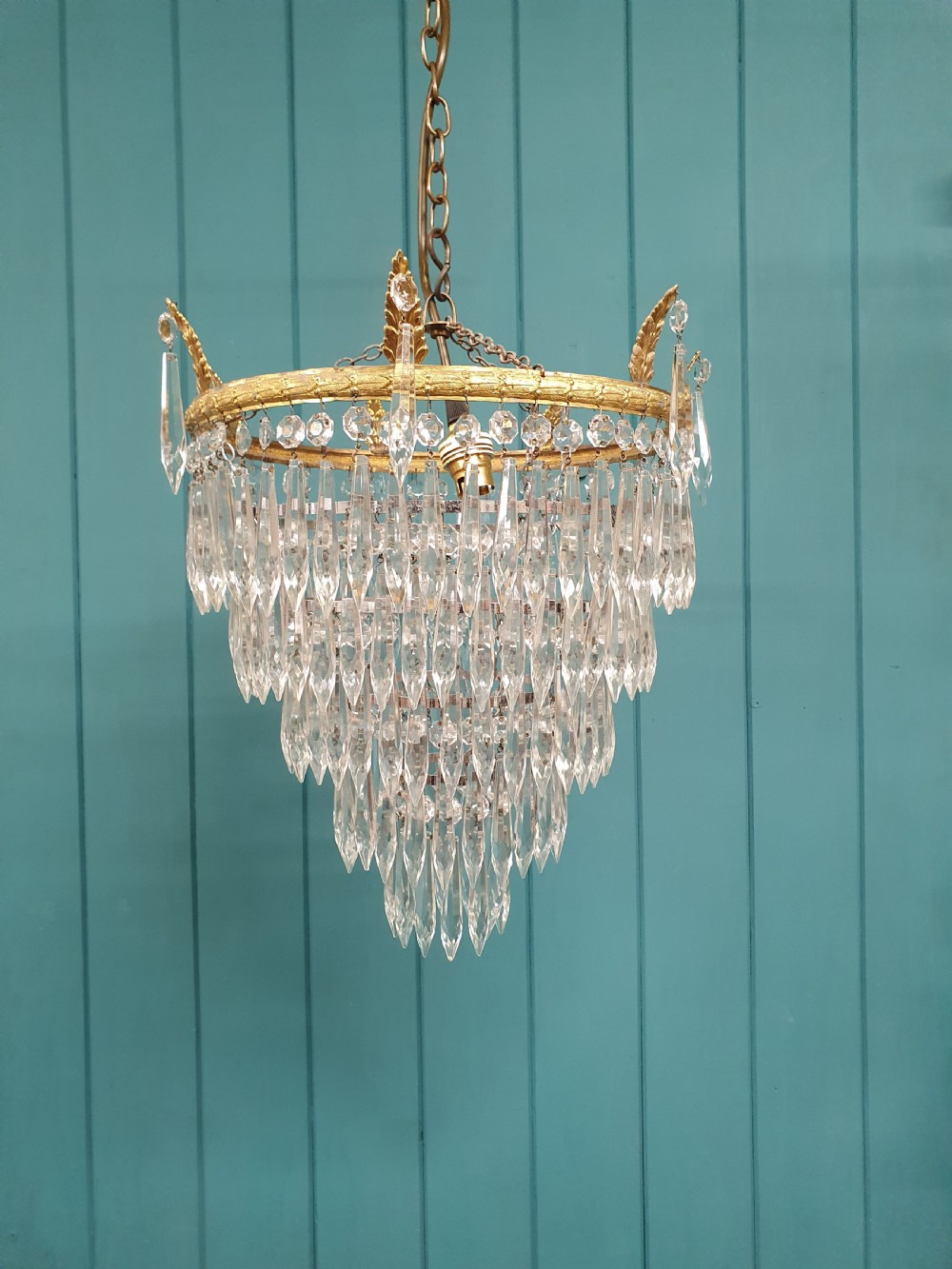 An early 20th-century chandelier with concentric tiers of clear crystal glass spikes suspended from a decorative gilt brass rim.