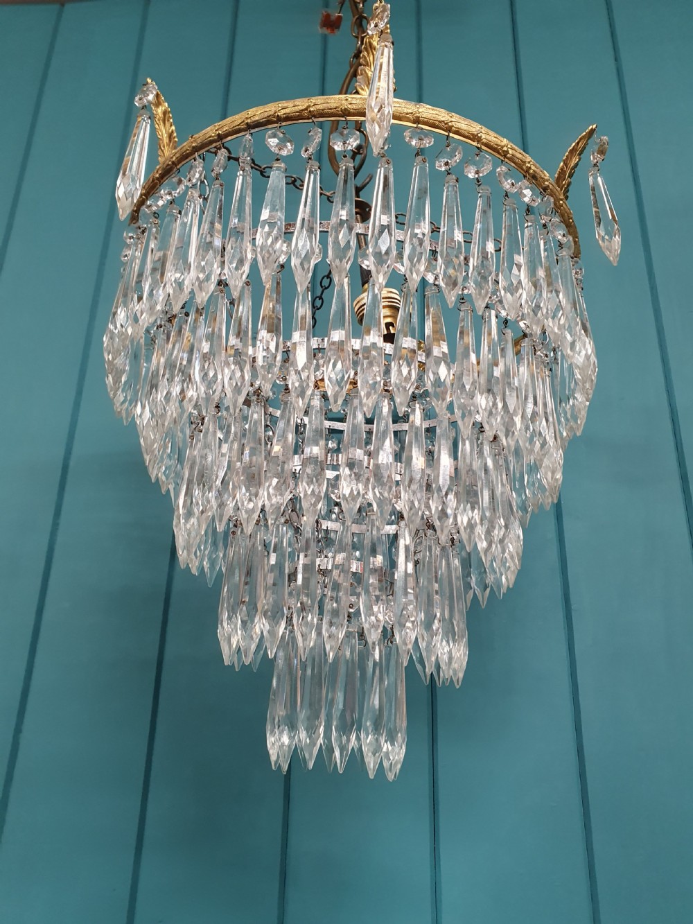 An early 20th-century chandelier with concentric tiers of clear crystal glass spikes suspended from a decorative gilt brass rim. View II