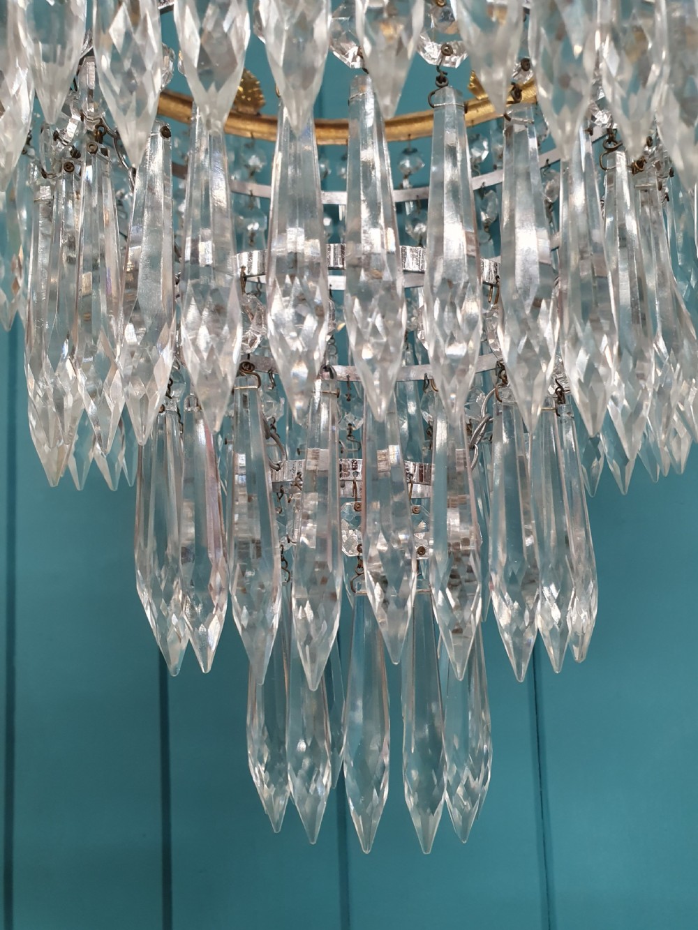 An early 20th-century chandelier with concentric tiers of clear crystal glass spikes suspended from a decorative gilt brass rim. View V