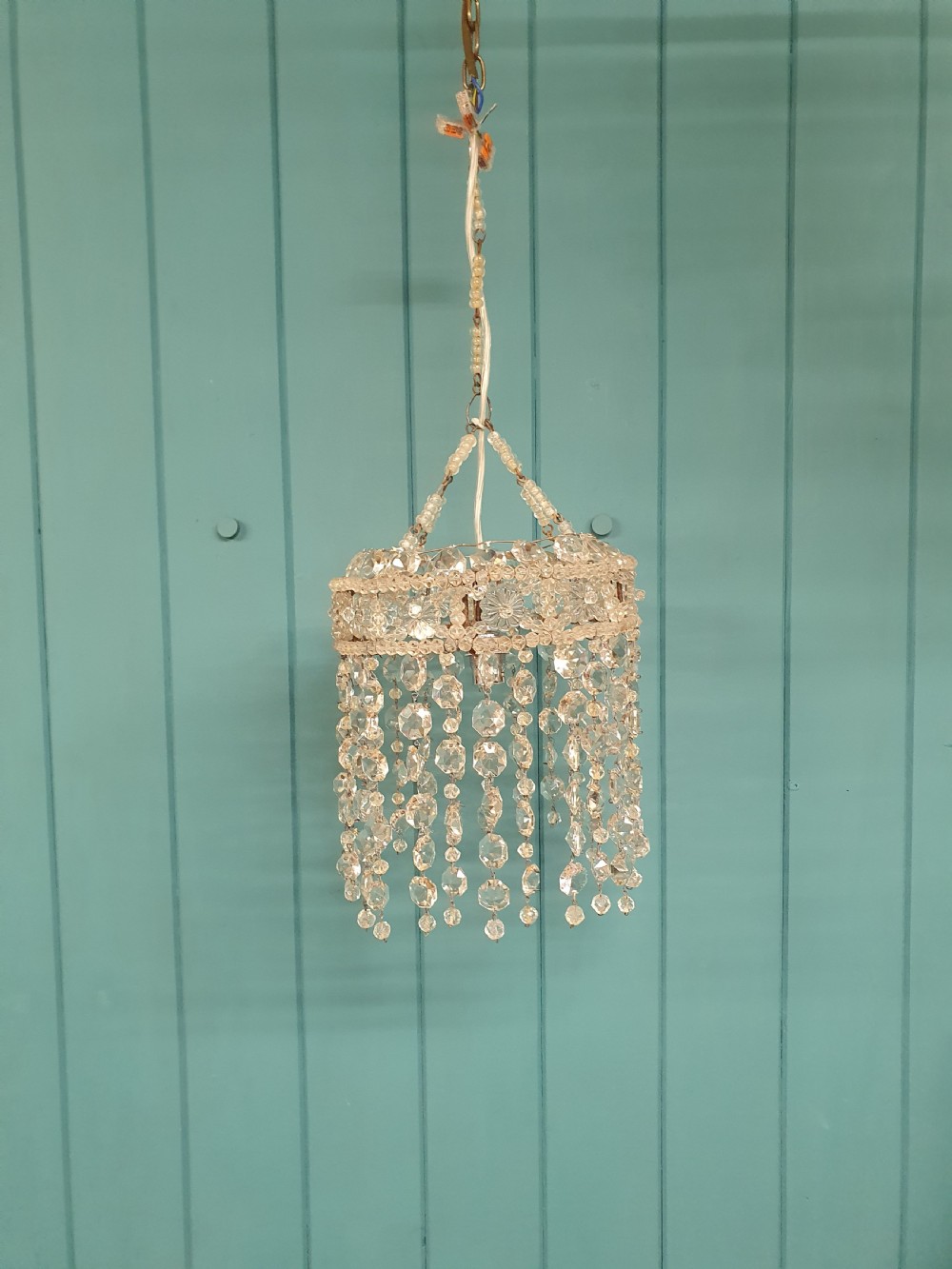 A small cylindrical ceiling light shade constructed from clear glass beads on a wire frame, featuring floral pattern bands and cascading faceted bead strands.